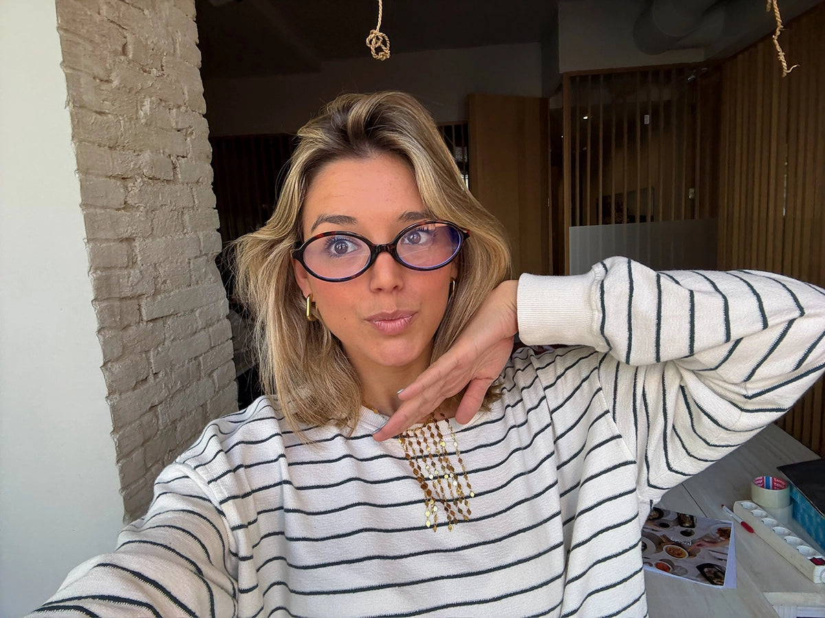Mujer joven con pendientes aro dorados de acero inoxidable, posando en interior con gafas y suéter a rayas.