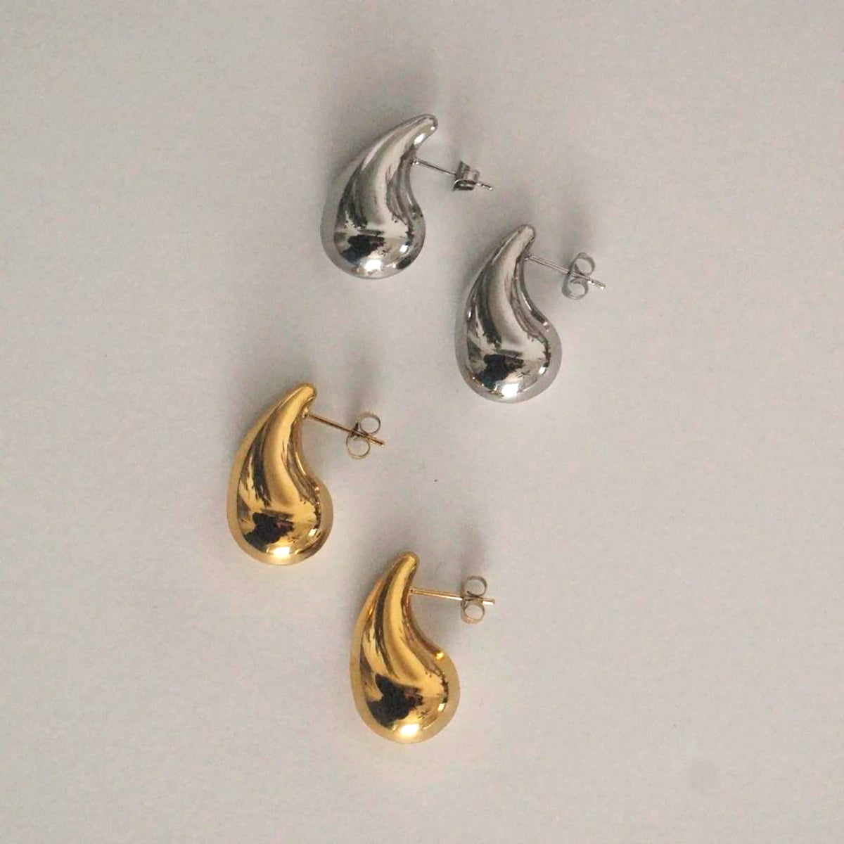 Pendientes de acero hipoalergénico en forma de gota, dorados y plateados, fondo claro.