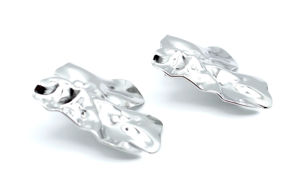 Pendientes Lys plateados de acero inoxidable en perspectiva lateral, diseño ondulado de superficie brillante, hipoalergénicos, resistentes al agua y duraderos - DELACABRA