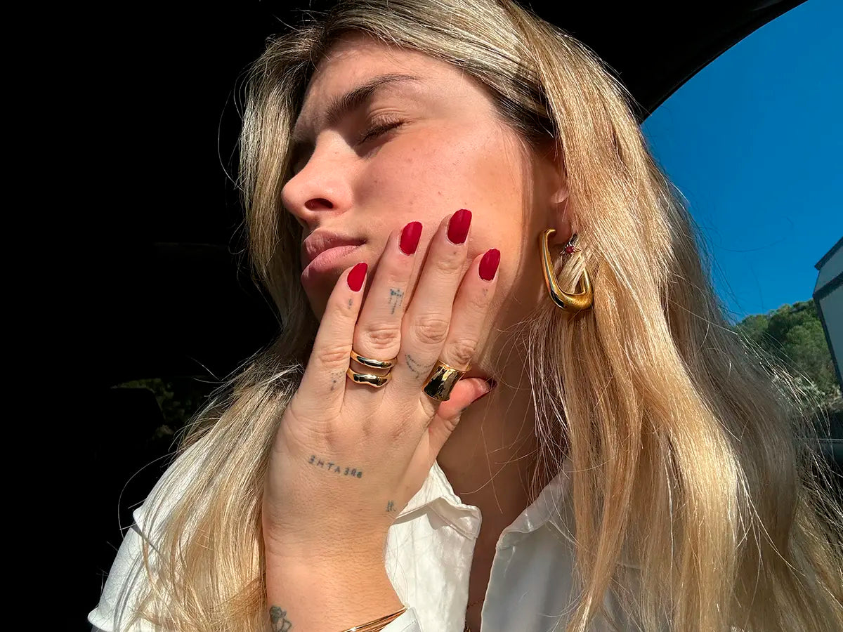 Pendientes Sunlight dorados con acabado pulido espejo, mujer luciendo los pendientes en conjunto con anillos de DELACABRA.COM acero inoxidable resistente al agua -DELACABRA