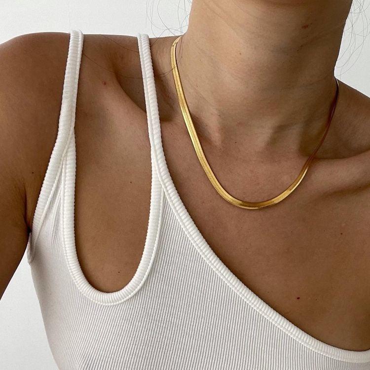 Collar dorado de acero inoxidable estilo plano, usado sobre top blanco de tirantes.