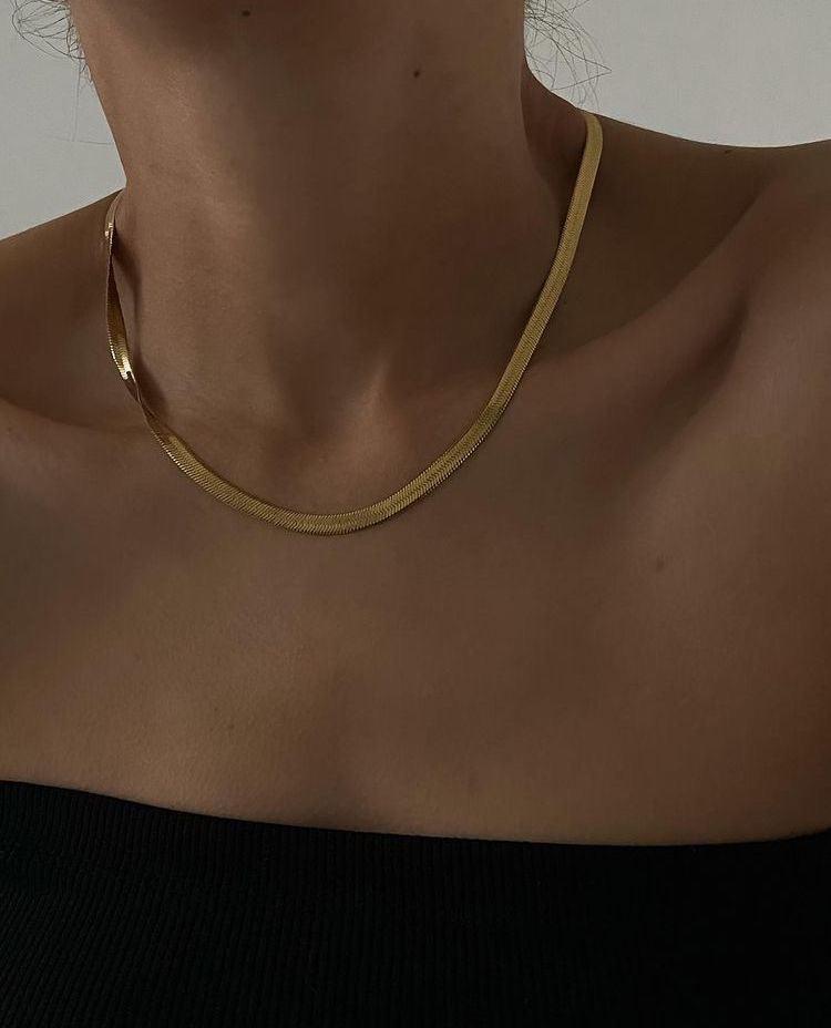 Collar de acero inoxidable dorado, diseño plano y elegante, sobre piel femenina.
