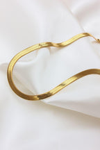 Collar de acero inoxidable dorado con diseño tipo serpiente sobre tela blanca.