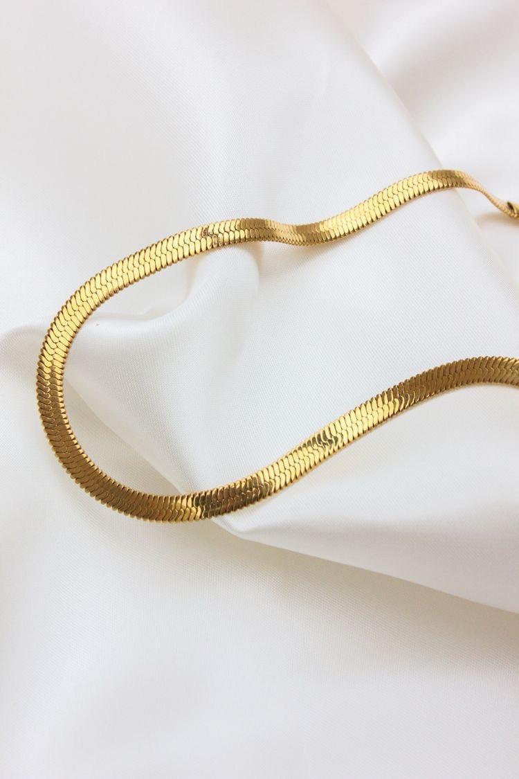Collar de acero inoxidable dorado con diseño tipo serpiente sobre tela blanca.