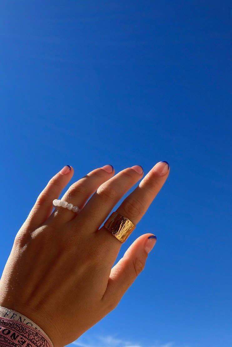 Anillo Gala dorado de mujer de acero inoxidable sobre dedo indice con fondo de cielo azul 